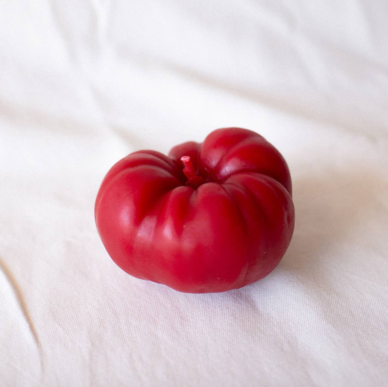 A red heirloom tomato candle made of beeswax, displayed on a white surface.