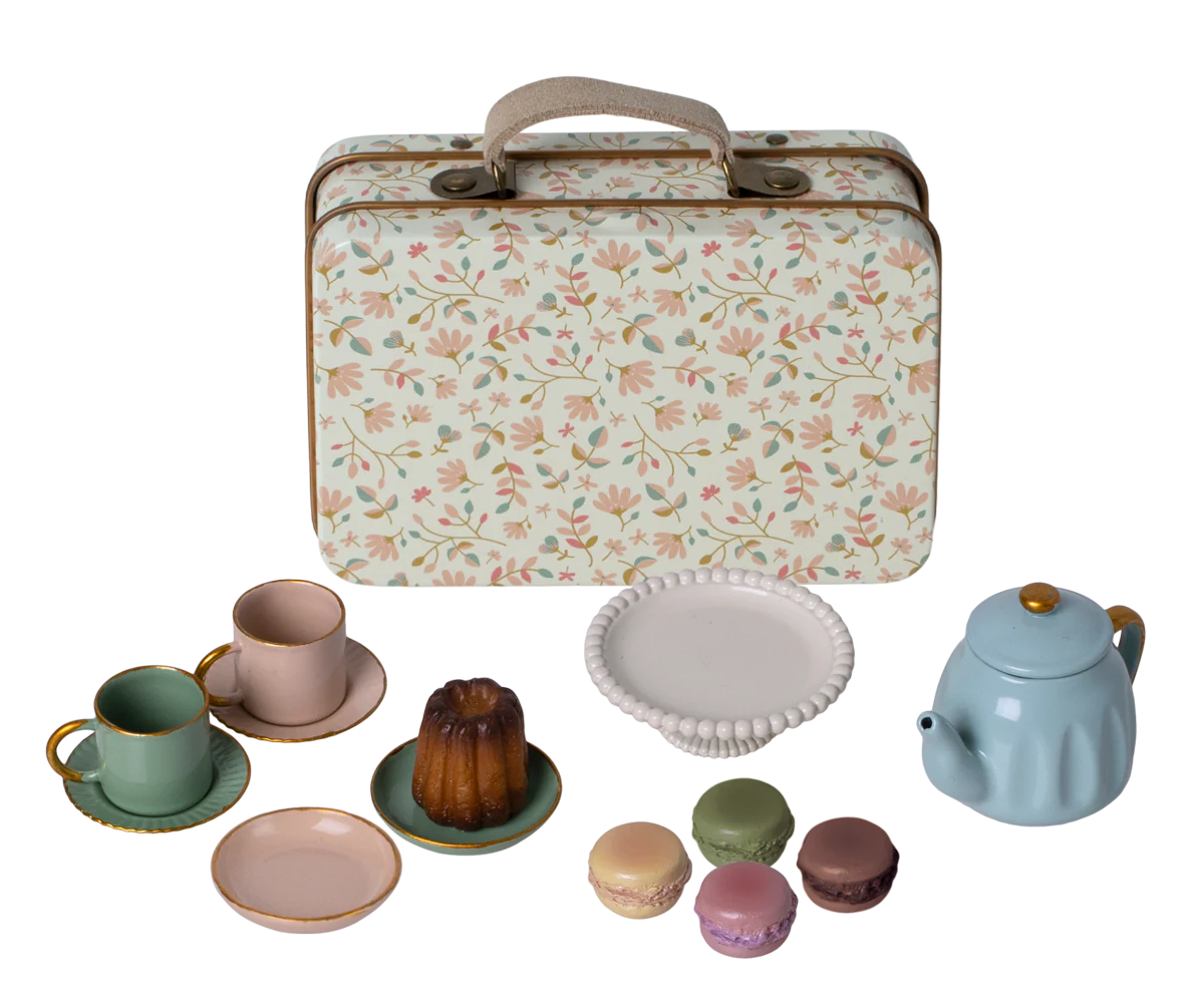 A metal suitcase with a floral pattern, accompanied by a tea set including cups, plates, and a teapot.