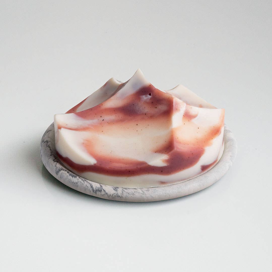 A creamy, swirled bar of soap with a smooth texture, predominantly white with swirls of pink and purple, presented on a grey dish.