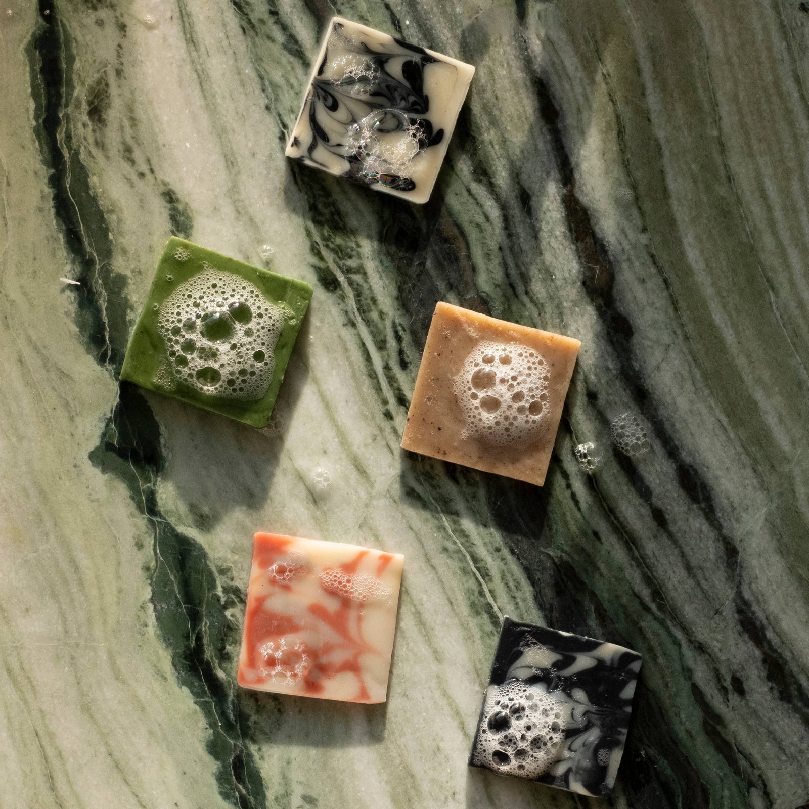 A selection of five different colored bars of soap arranged on a marble surface, each with a distinctive pattern and color.