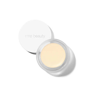 A small glass pan of RMS Beauty UnCoverup Concealer with a white cap that says "RMS Beauty,"