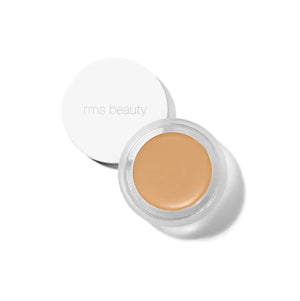 A small glass pan of RMS Beauty UnCoverup Concealer with a white cap that says "RMS Beauty,"
