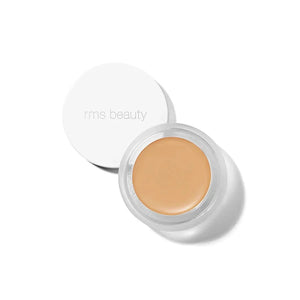 A small glass pan of RMS Beauty UnCoverup Concealer with a white cap that says "RMS Beauty,"