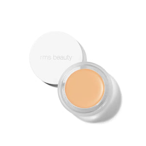 A small glass pan of RMS Beauty UnCoverup Concealer with a white cap that says "RMS Beauty,"