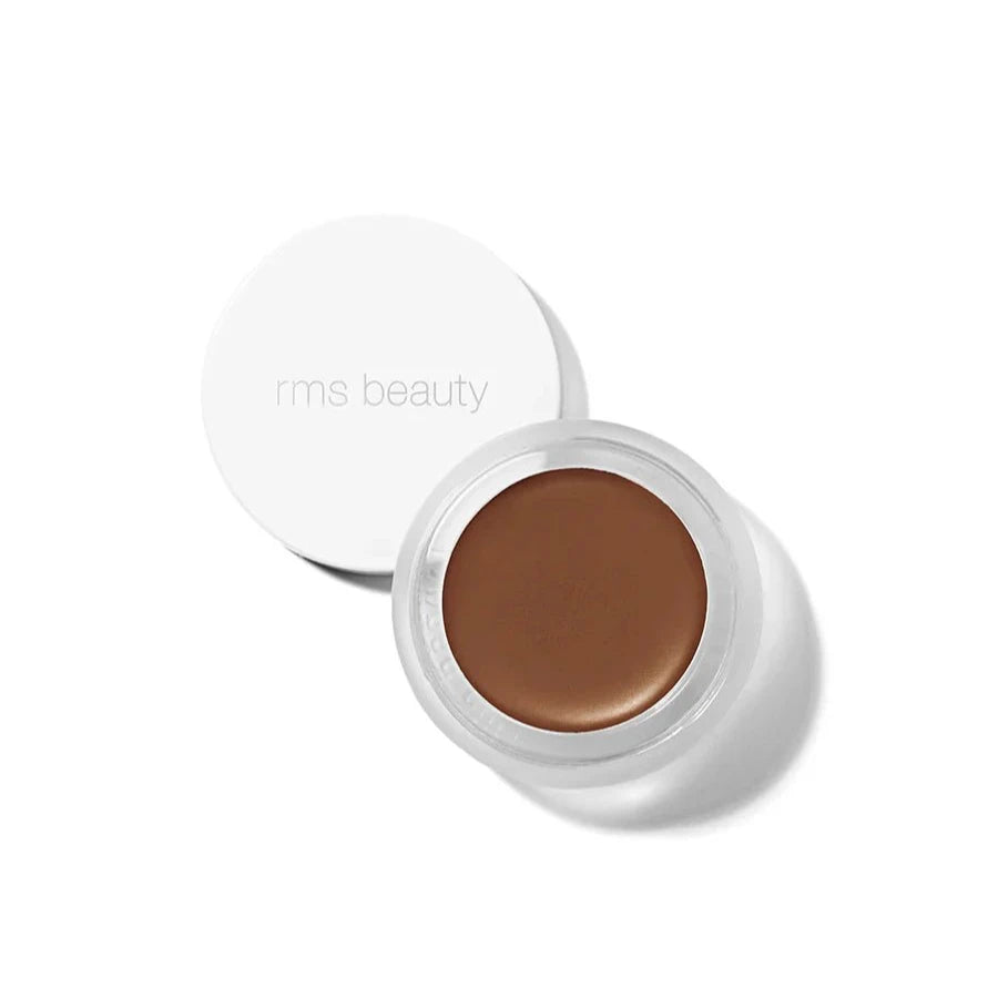 A small glass pan of RMS Beauty UnCoverup Concealer with a white cap that says "RMS Beauty,"
