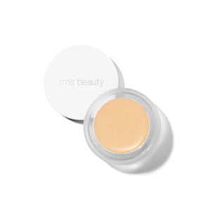 A small glass pan of RMS Beauty UnCoverup Concealer with a white cap that says "RMS Beauty,"