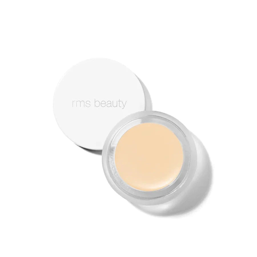 A small glass pan of RMS Beauty UnCoverup Concealer with a white cap that says "RMS Beauty,"