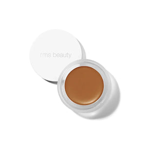 A small glass pan of RMS Beauty UnCoverup Concealer with a white cap that says "RMS Beauty,"