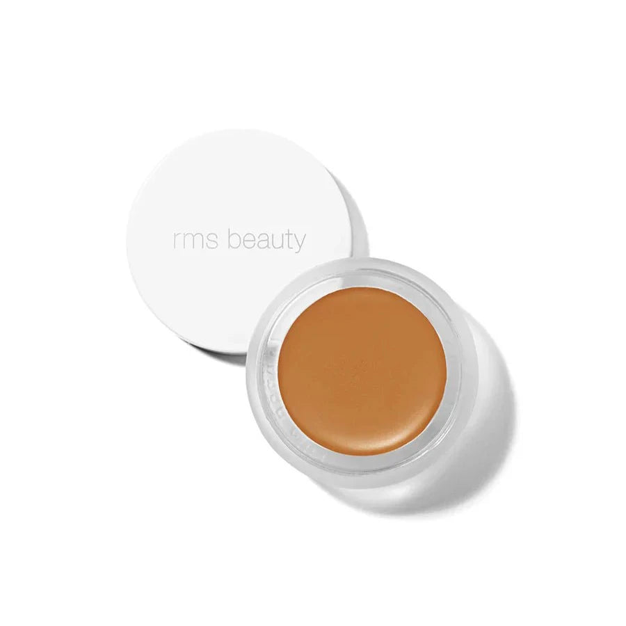 A small glass pan of RMS Beauty UnCoverup Concealer with a white cap that says "RMS Beauty,"