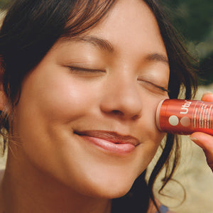A person applying a tube of UTU outdoor sunscreen to their face