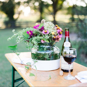 A white color block vase on a table in a green setting. 