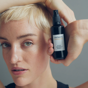 A woman with short blonde hair holding a bottle of Vintner's Daughter Active Treatment Essence to her face. 
