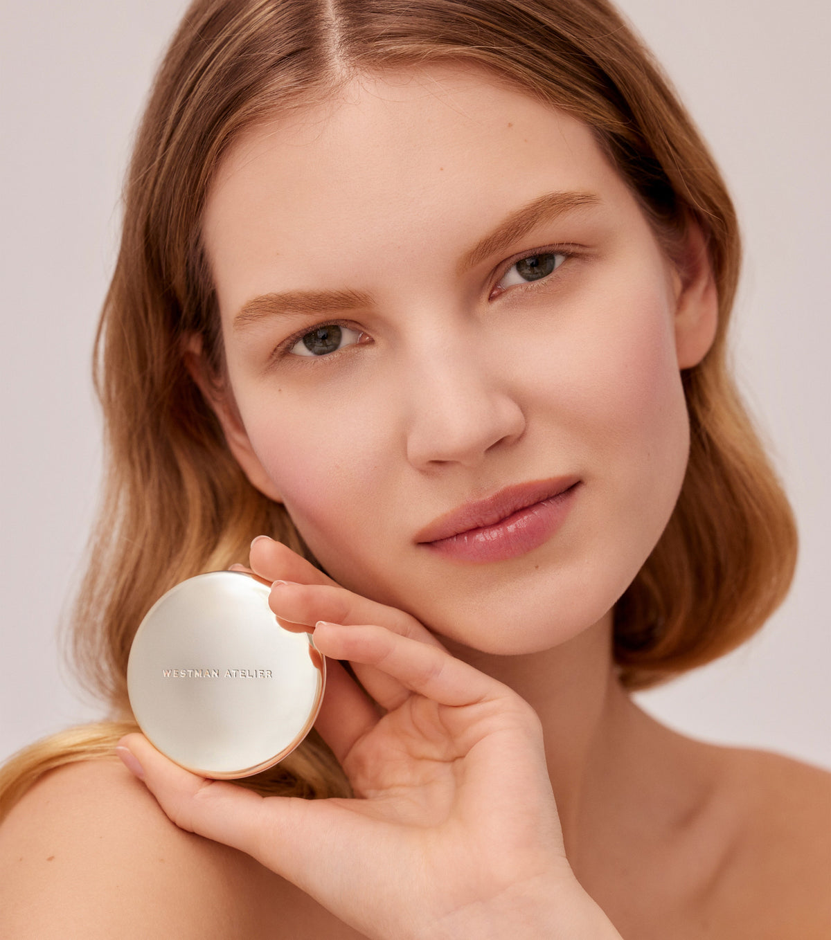 Woman holding a compact mirror with a neutral background