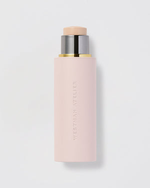 A stick of Westman Atelier Vital Skin Foundation with a pale pink tone, packaged in a sleek, cylindrical container.