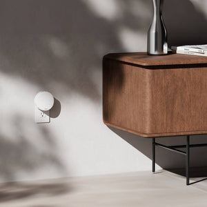 Wooden sideboard with a wall-mounted lamp in a minimalistic room.