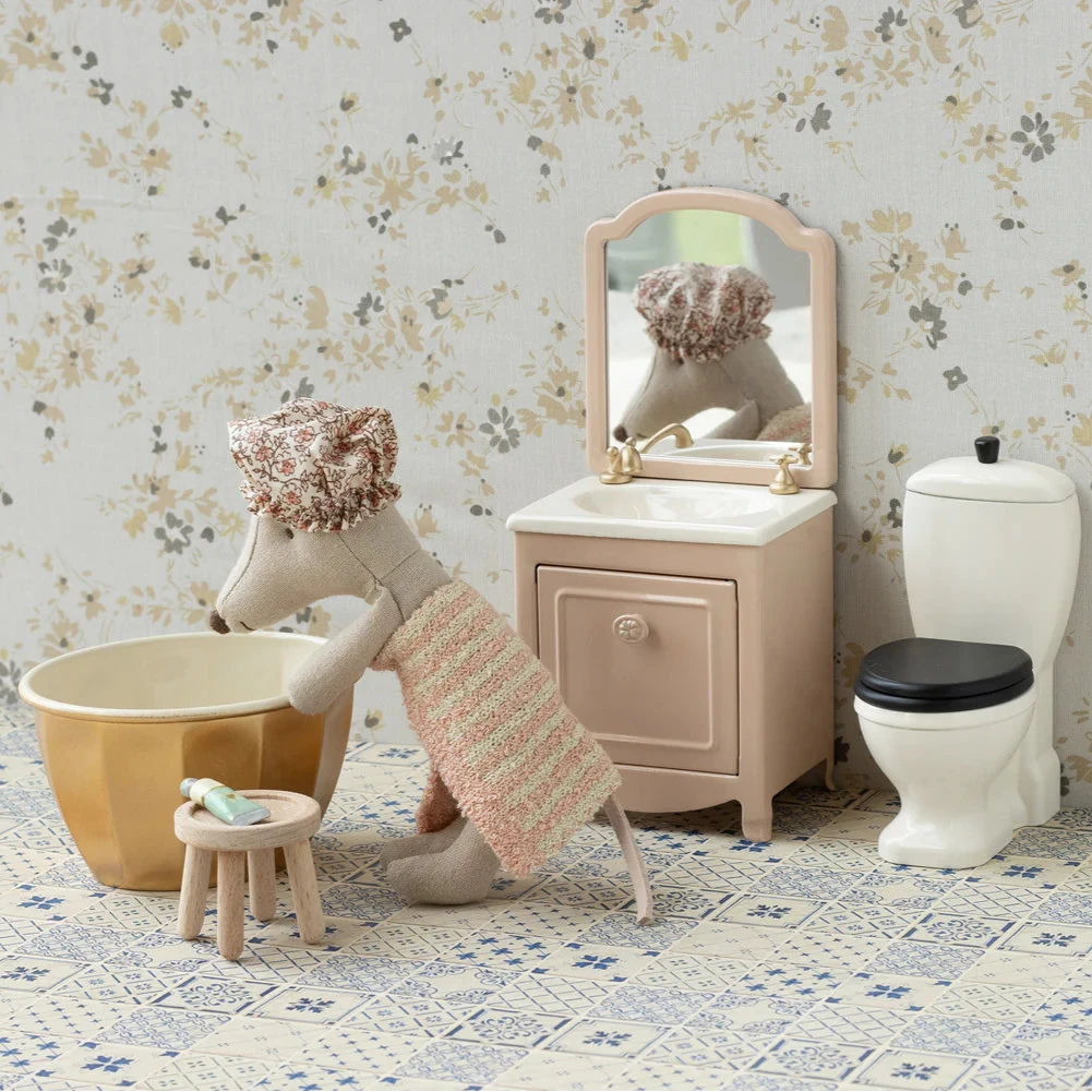 Bathroom setting with a toy dog, sink, and toilet against a floral wallpaper background.