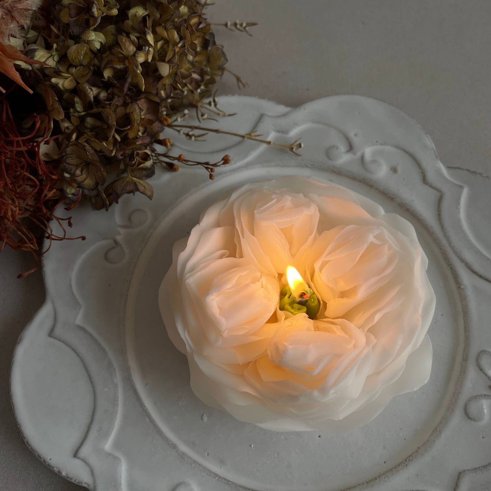 Floral candle on a decorative plate with dried flowers in the background