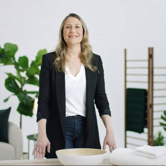 Woman standing in a modern living room with plants and furniture.