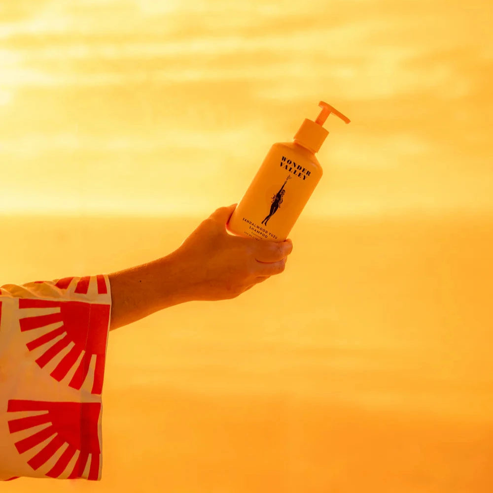 A person holding a bottle of the Sandalwood Yuzu hair shampoo, made by Wonder Valley in California