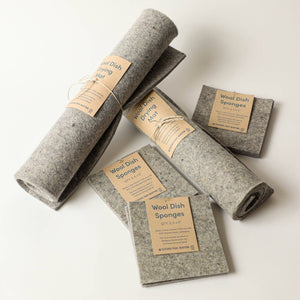 A group of wool dish sponges and wool dish drying mats, on a light grey surface. 