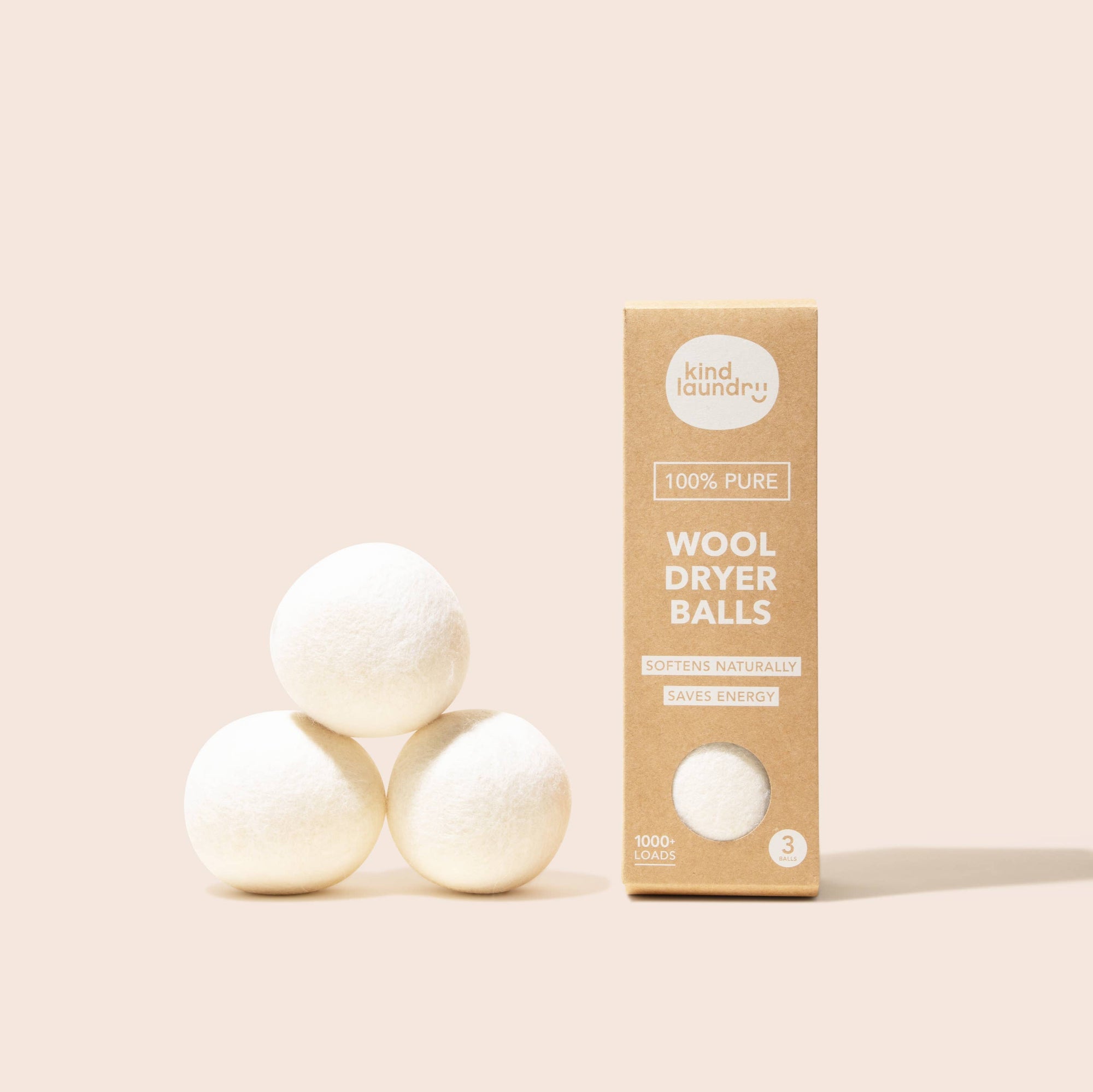 Three white wool dryer balls next to a beige package labeled 'Wool Dryer Balls' by Kind Laundry.