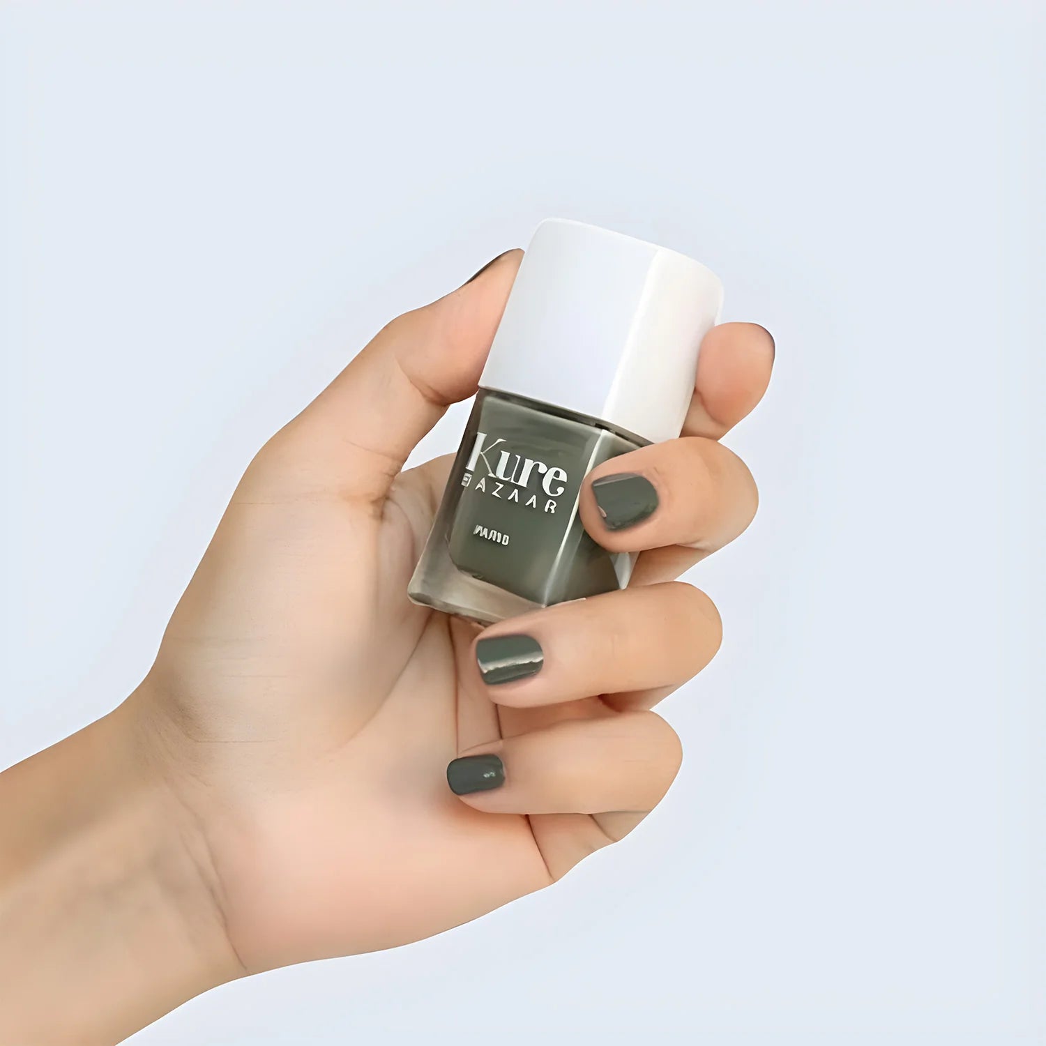 A hand holding a bottle of kure bazaar nail polish in a green color. 